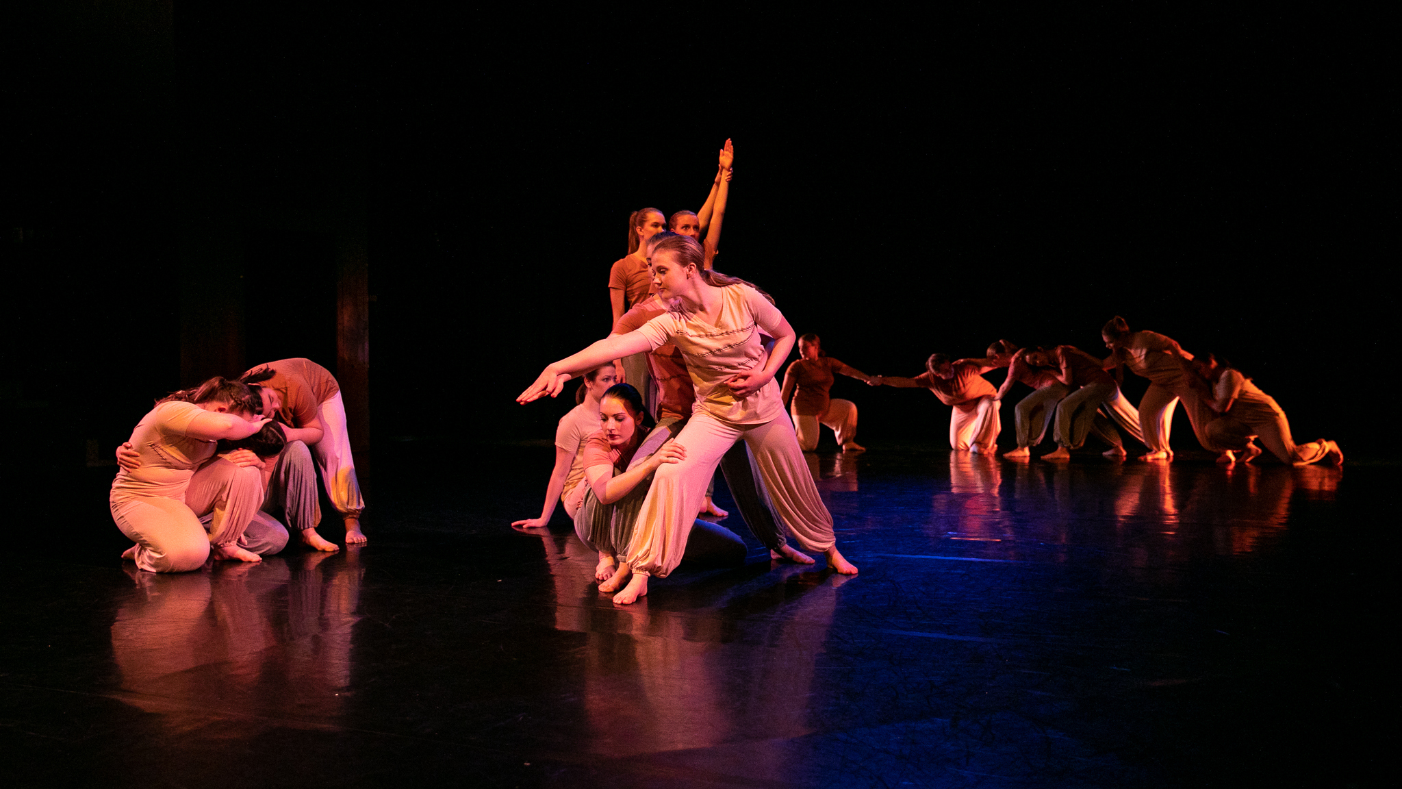 A group of dancers on a stage. Two dancers huddled together, several dancers holding hands
