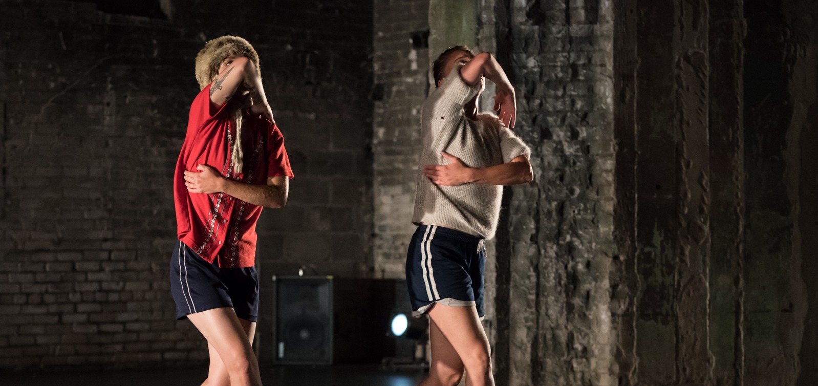 Two dancers standing, gesturing one arm across the chest and the other arm across the face