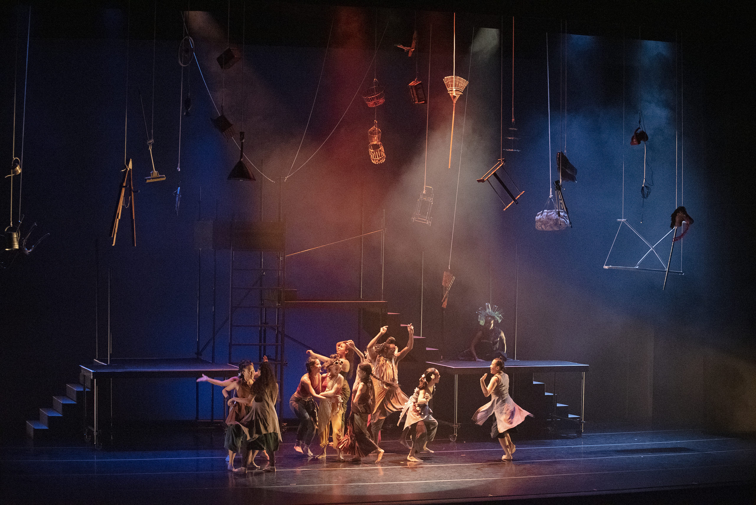 A group of dancers on a stage with several household items suspended above them