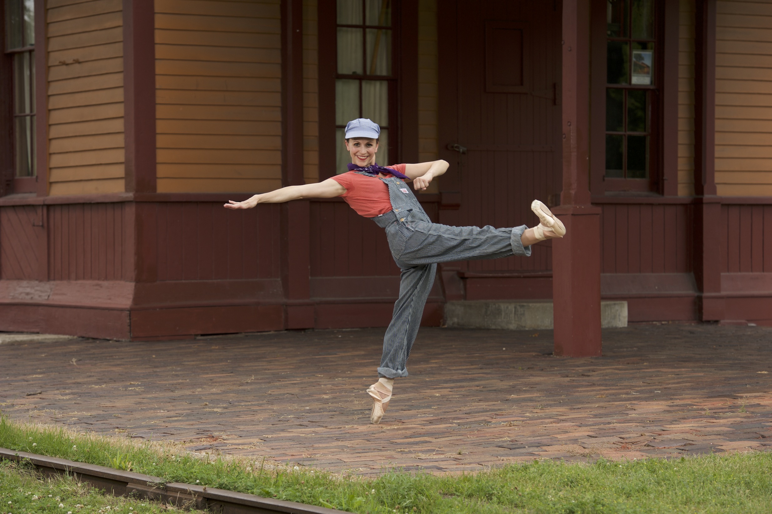 Dancer en point near a train station, dressed like a train conductor