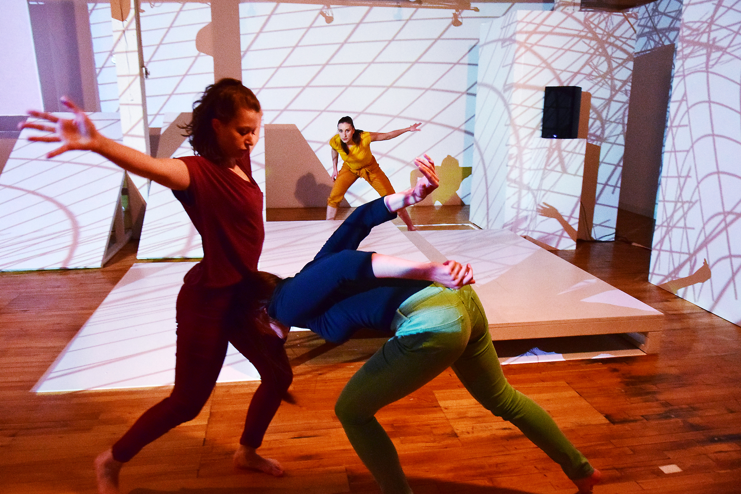 Three dancers in a room with a grid of shadows