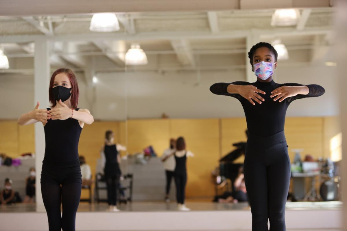 Several dancers in dark clothes dance for a circle in the TU Dance main studio