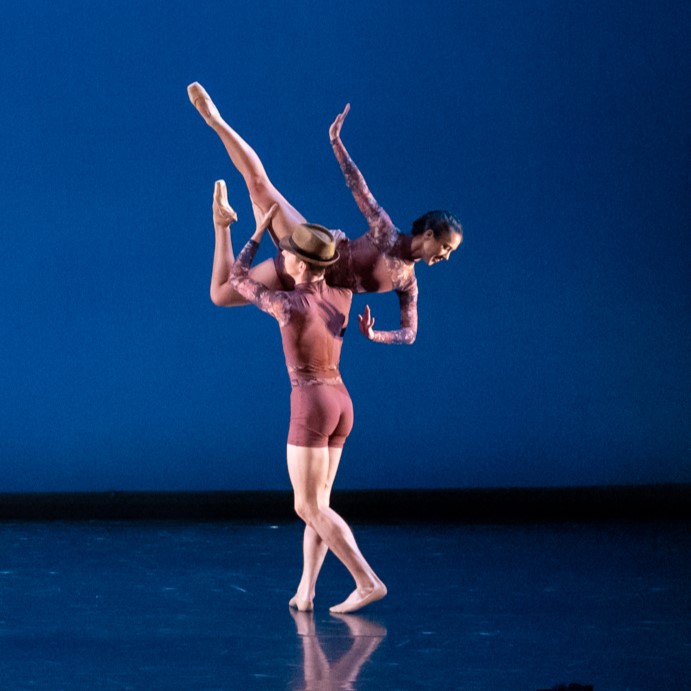 Two dancers in purple biketards with flowered sleeves are dancing together.
