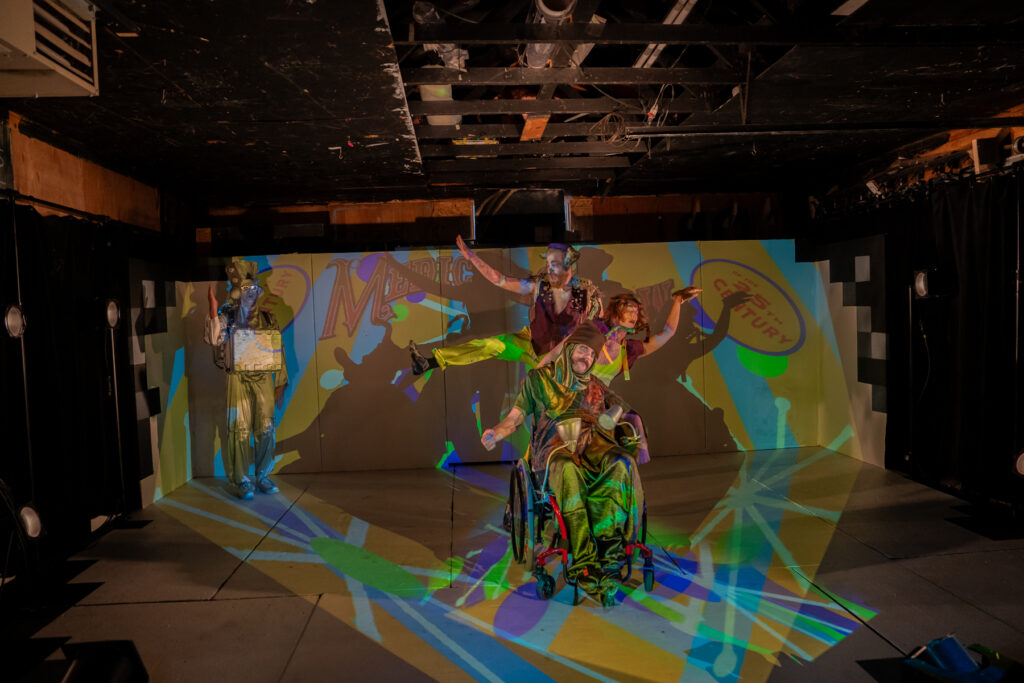 Medicine show cast in formation with bright visuals projected on them and the set.